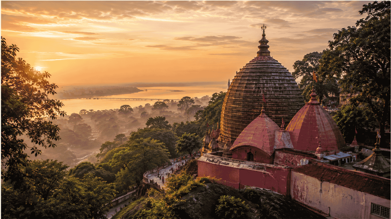 This panoramic image captures the Kamakhya Devi Temple bathed in the golden light of dawn atop Nilachal Hill in Guwahati, Assam. Surrounded by lush forests and overlooking the majestic Brahmaputra River, the temple's distinctive Nilachal-style dome and reddish-pink architecture stand as symbols of one of Hinduism's most sacred pilgrimage sites. Believed to mark the Yoni Peetha of Goddess Sati, Kamakhya Temple is an important center of Shakta philosophy, Tantra, and the world-famous Ambubachi Mela, attracting millions of devotees and spiritual seekers every year.