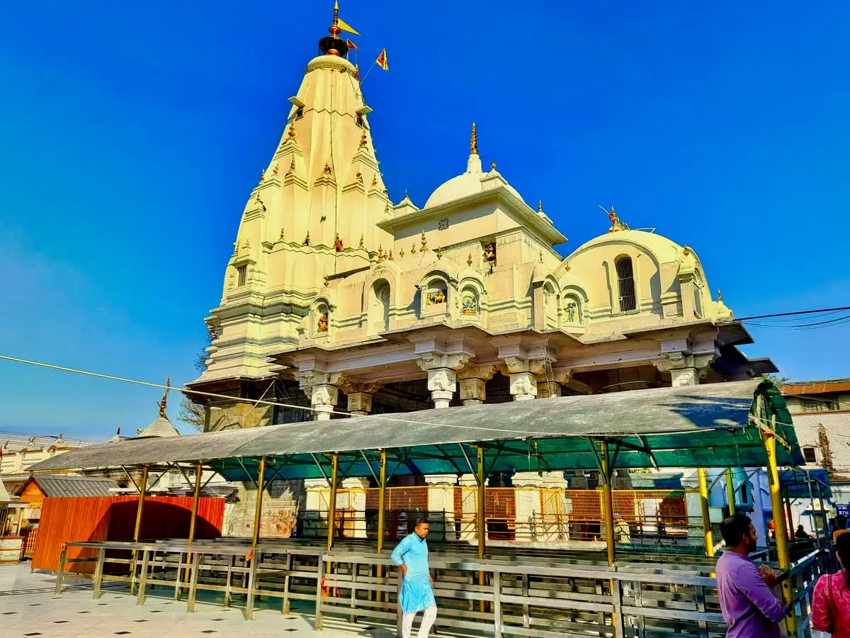 Cream-coloured shikhara and domes of Brajeshwari Devi temple above a covered pilgrim queue