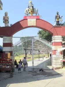 Red and white entrance arch topped with Shiva figures at Chamunda Devi temple near Palampur