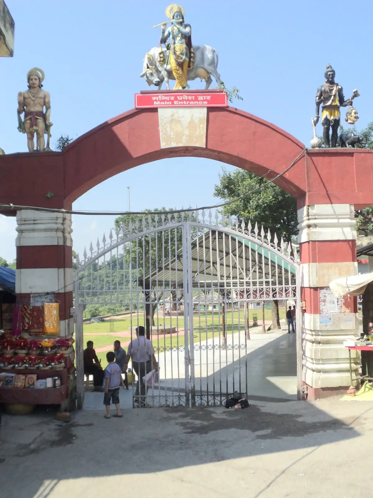 Red and white entrance arch topped with Shiva figures at Chamunda Devi temple near Palampur