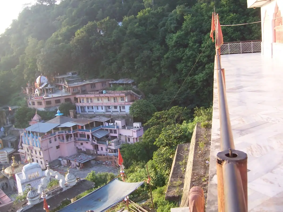 Pink and white temple buildings of Jwalamukhi town on a forested hillside in Kangra