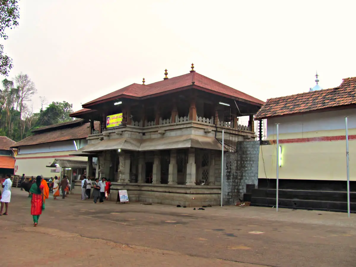 Brass lamp tower and gold-clad dhwaja stambha before the stone-roofed Mookambika shrine at Kollur
