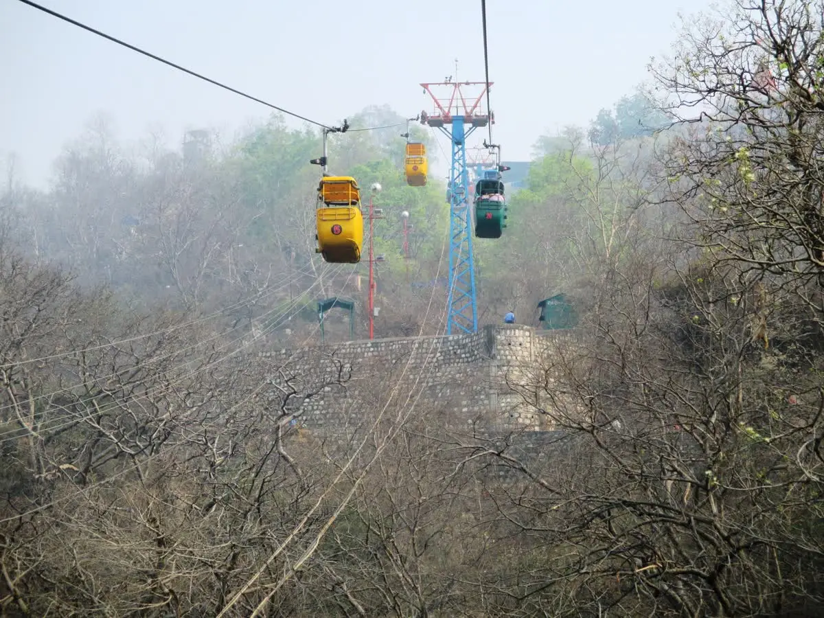 Yellow and green cable cars of the Mansa Devi ropeway above a wooded Haridwar hillside