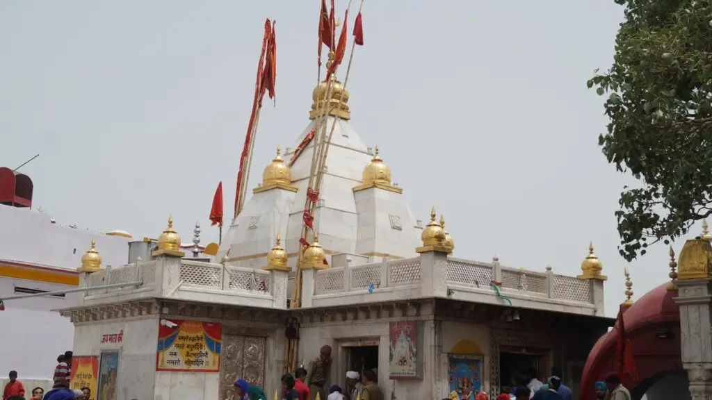 White marble Naina Devi temple with golden finials and pilgrims gathered in the courtyard