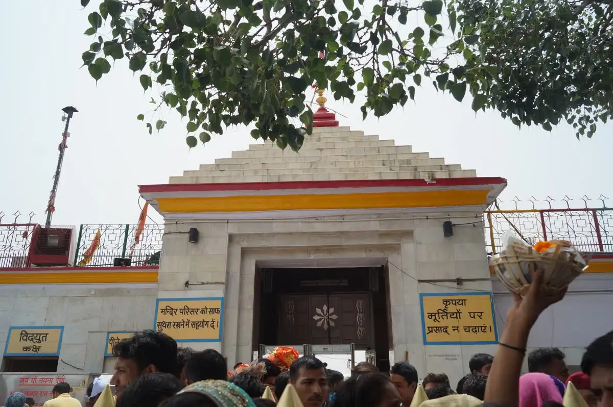 Stepped white shikhara above the Naina Devi temple entrance with pilgrims waiting below